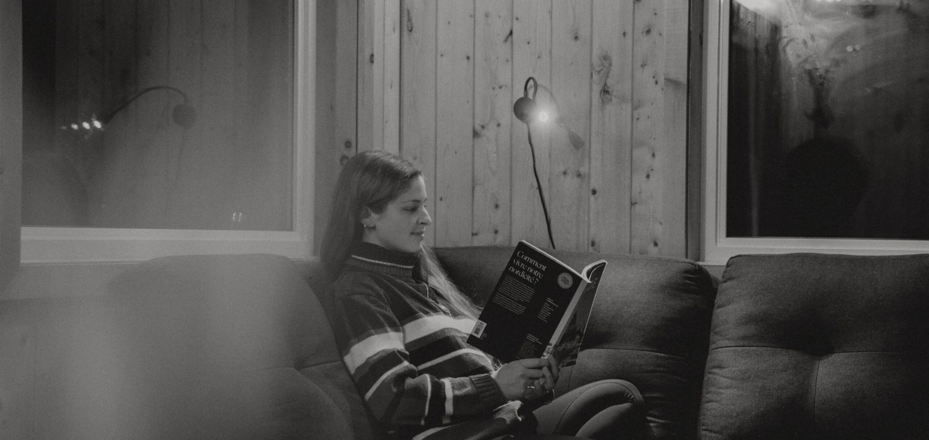 Une femme qui boit une coupe de vin et lit un livre à l'intérieur du confort de notre chalet à Gaspé.